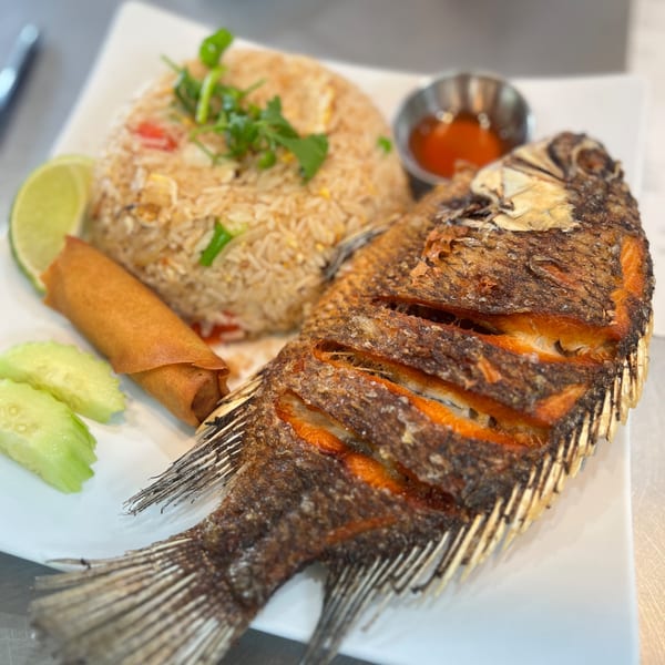 Crispy fried whole fish with fried rice, spring roll, lime, and cucumber on a white plate.