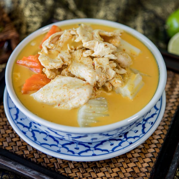 Proud Thai yellow curry with chicken, carrots, and potatoes in a white and blue bowl.