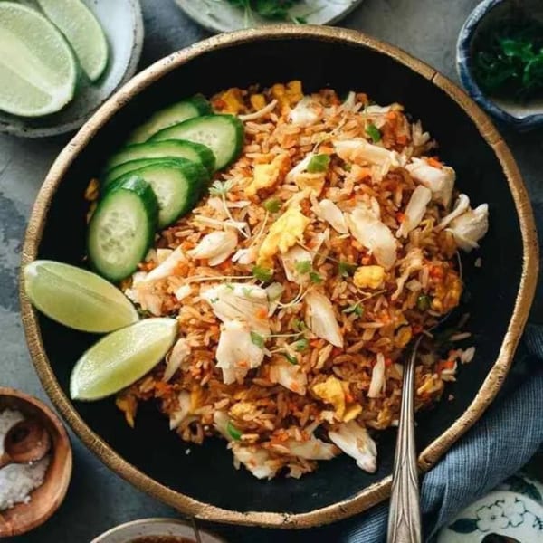 Proud Thai's crab fried rice with cucumber slices and lime wedges in a black bowl.